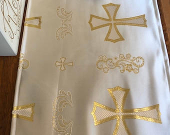 May include: A white table runner with gold embroidered crosses and floral designs. The runner is made of a soft, silky fabric.
