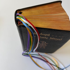 K&ouml;nnte beinhalten: Ein schwarzes, ledergebundenes Buch mit goldener Aufschrift "St. Joseph Daily Missal". Das Buch hat mehrere farbige Lesezeichen aus Band.