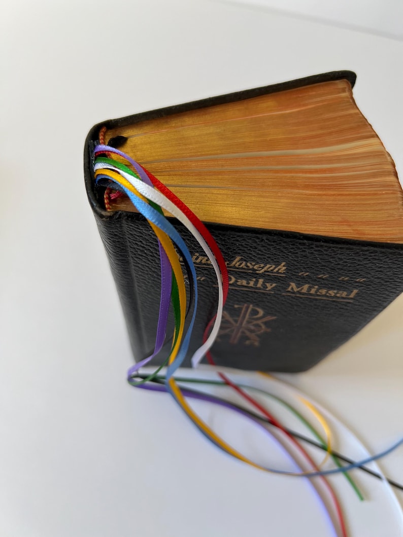 K&ouml;nnte beinhalten: Ein schwarzes, ledergebundenes Buch mit goldener Aufschrift "St. Joseph Daily Missal". Das Buch hat mehrere farbige Lesezeichen aus Band.