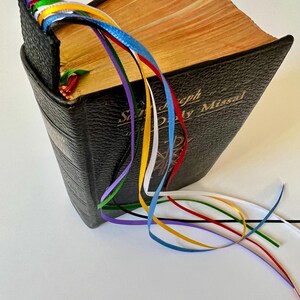 K&ouml;nnte beinhalten: Ein schwarzes, ledergebundenes Buch mit einem goldenen Titel, "Saint Joseph Daily Missal", und einem Lesezeichen mit mehreren bunten B&auml;ndern.