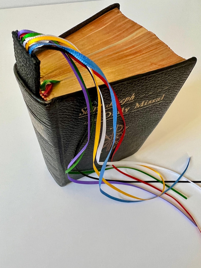 K&ouml;nnte beinhalten: Ein schwarzes, ledergebundenes Buch mit einem goldenen Titel, "Saint Joseph Daily Missal", und einem Lesezeichen mit mehreren bunten B&auml;ndern.