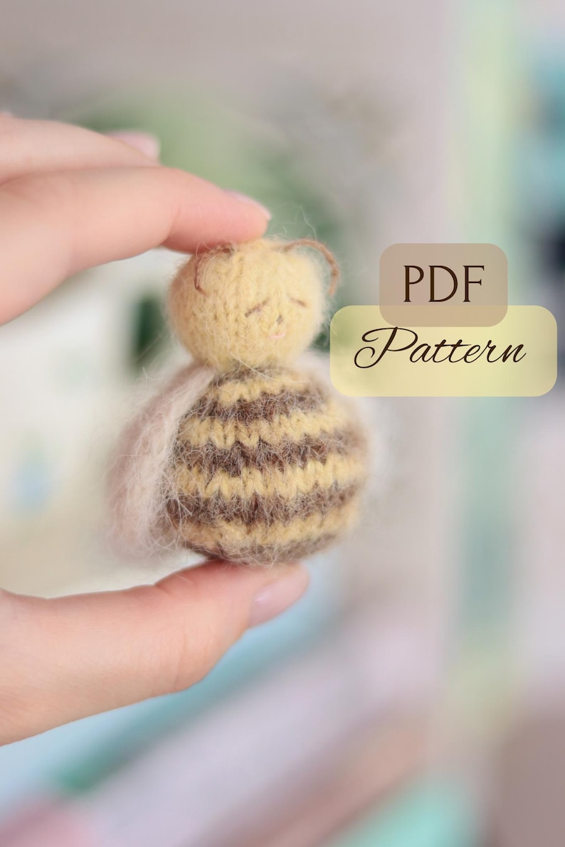 Pode incluir: Uma pequena boneca em forma de abelha, feita &agrave; m&atilde;o, com cabe&ccedil;a amarela e corpo listrado marrom e bege. A imagem inclui o texto "PDF Pattern". A boneca &eacute; segurada em uma m&atilde;o.