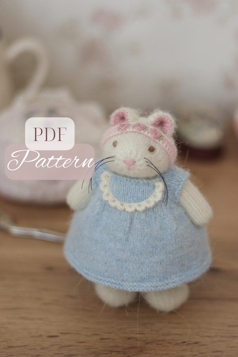 May include: A handmade white stuffed bunny wearing a light blue dress with a white lace collar and a pink hat with floral accents. The bunny has black whiskers and a pink nose. The image has the text "PDF Pattern".