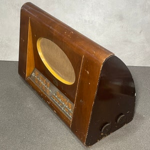 May include: A vintage wooden radio with a curved design. The radio has a dark brown finish with a lighter wood oval speaker grill. The front panel has a clear display with orange markings and two knobs on the side.