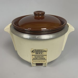 May include: An off-white Cordon Bleu automatic slow cooker with a brown ceramic lid. The slow cooker has a silver rim and a control panel with settings for Auto, Low, and High. A vintage kitchen appliance.
