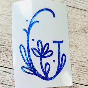 May include: A blue glitter vinyl decal with a floral design and the letter G. The decal is on a white background.