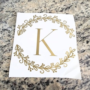 May include: Gold vinyl decal with a wreath of leaves and the letter K in the center.