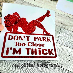 May include: A red glitter holographic decal featuring a reclining woman silhouette and the text "DON'T PARK Too Close i'M THICK". The decal is on a white background.