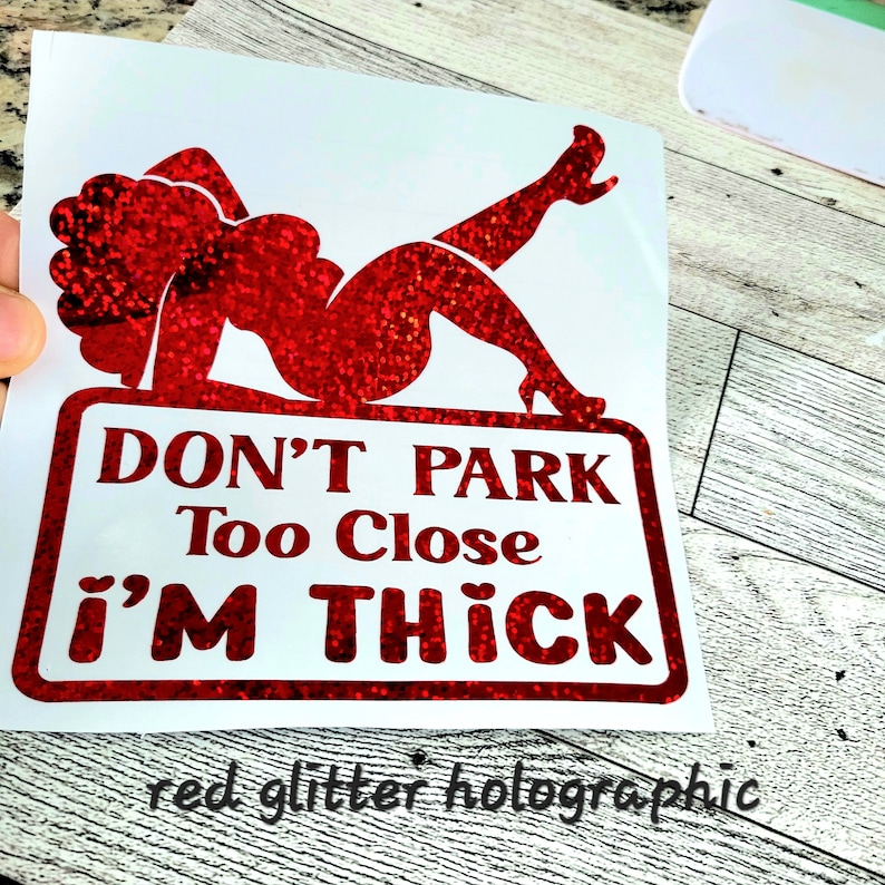 May include: A red glitter holographic decal featuring a reclining woman silhouette and the text "DON'T PARK Too Close i'M THICK". The decal is on a white background.