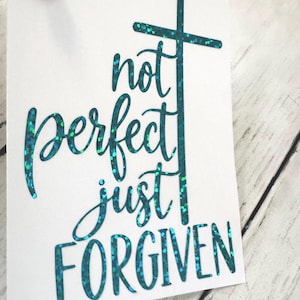 May include: A white rectangular card featuring the teal glitter text "not perfect just FORGIVEN" with the letter "t" in "not" stylized as a cross. The card is held by a silver clip with a white pearl accent at the top corner of the card.