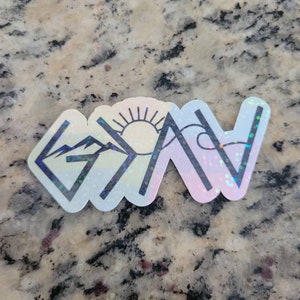 May include: A holographic sticker with a mountain range, a sun, and a wave design. The sticker has a white background and black outlines. The text "God is Now" is written in black letters.