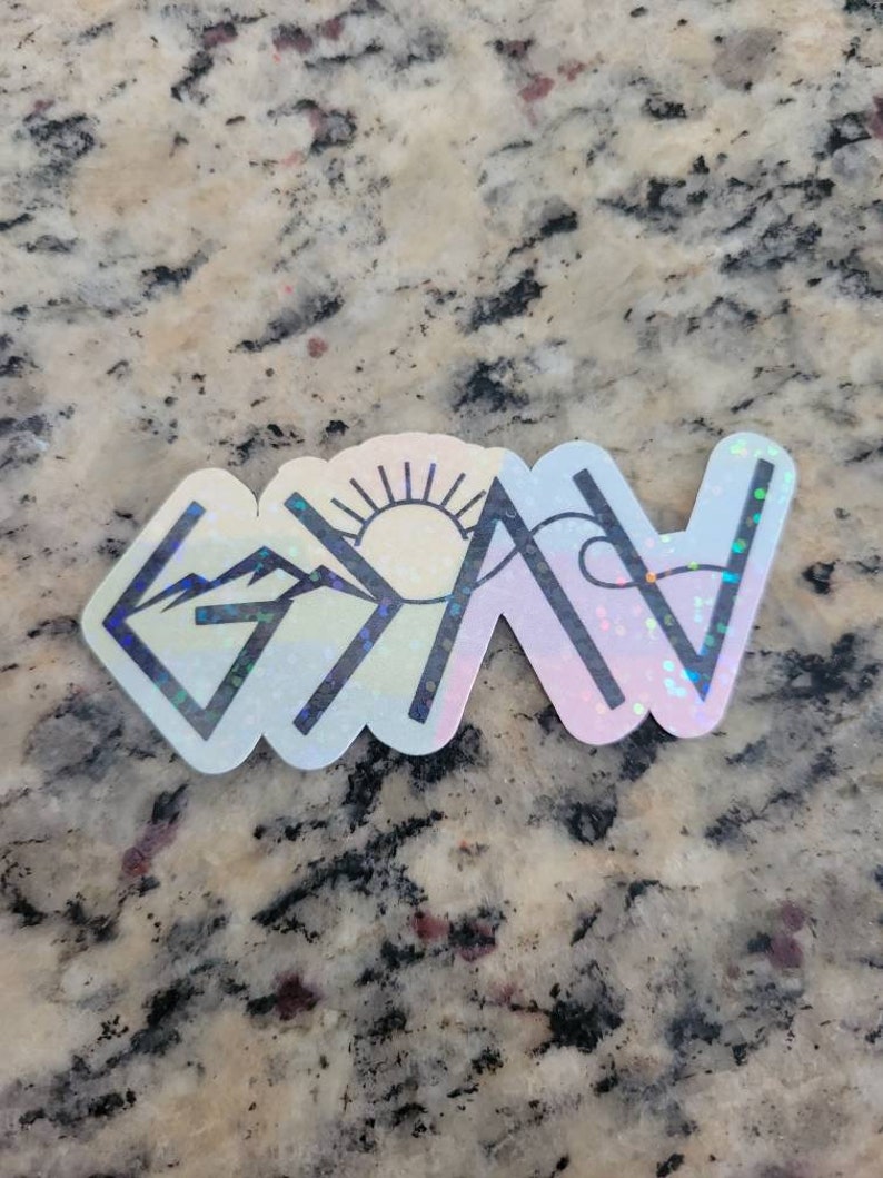 May include: A holographic sticker with a mountain range, a sun, and a wave design. The sticker has a white background and black outlines. The text "God is Now" is written in black letters.