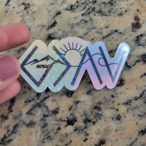 May include: A holographic sticker with a mountain range, sun, and the word "Grateful" in a stylized font.