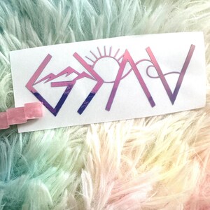 May include: A white sticker with the word "GOAV" in a gradient pink and purple color scheme. The letters are stylized with mountain and sun designs. The sticker is on a fluffy, rainbow-colored surface.