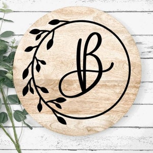 May include: A round wooden sign with a black wreath and the letter "B" in a cursive font.