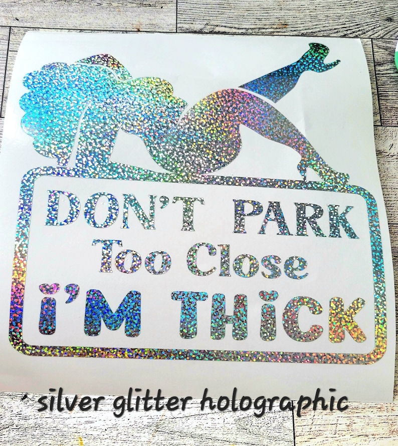 May include: Silver glitter holographic sticker with a graphic of a woman reclining on a sign that reads "DON'T PARK Too Close I'M THICK". The sticker also has the text "silver glitter holographic".