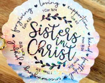 May include: A white and iridescent sticker with a watercolor background and glitter. The sticker says "Sisters in Christ" with bible verses around the edge. The verses are: 1 Cor. 16:14, Gal. 6:2, Prov. 16:24, Rom. 12:12, 1 Thes. 5:11, Prov. 20:6.