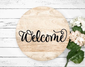 May include: A round wooden sign with the word "Welcome" written in black cursive script. The sign is on a white wooden background with white and pink flowers.