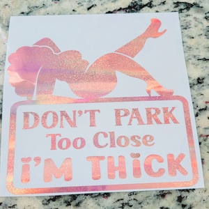 May include: A white sticker with a pink glitter design of a woman reclining on a sign. The sign reads "DON'T PARK Too Close I'M THICK" in pink glitter lettering.