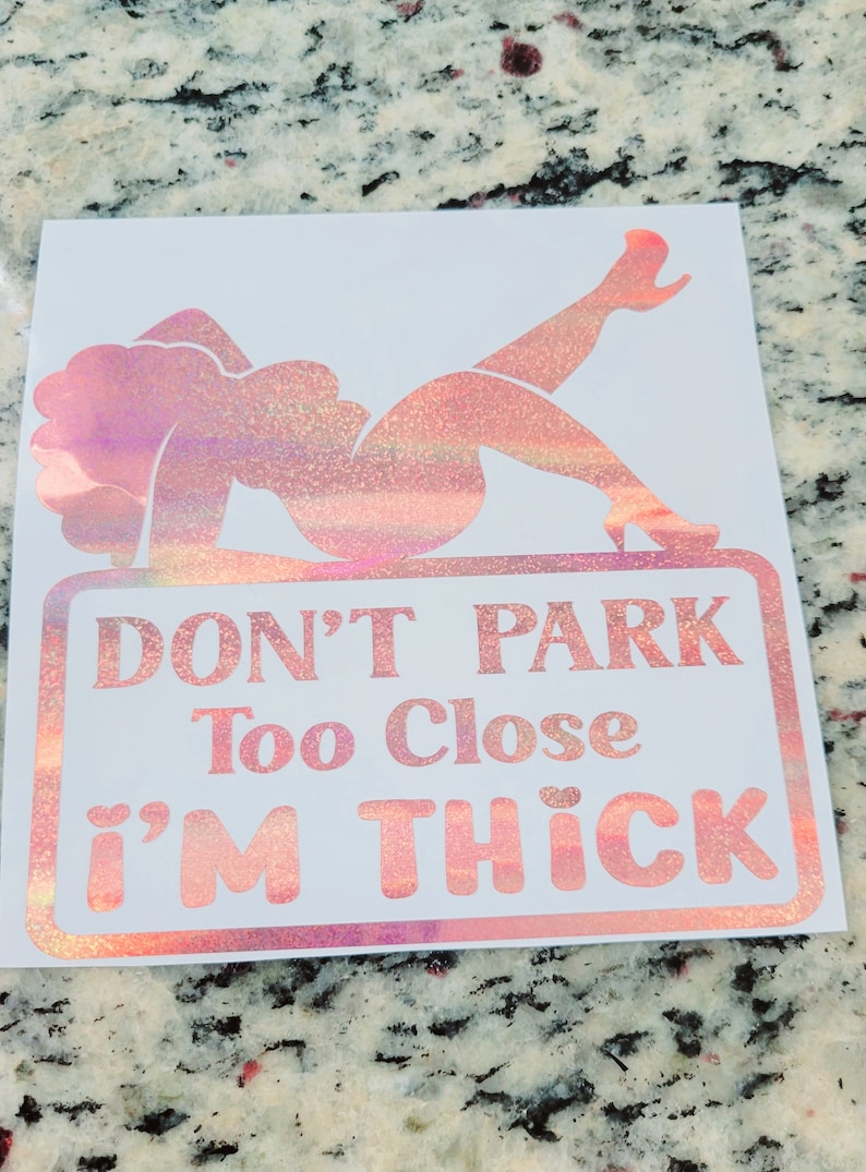 May include: A white sticker with a pink glitter design of a woman reclining on a sign. The sign reads "DON'T PARK Too Close I'M THICK" in pink glitter lettering.