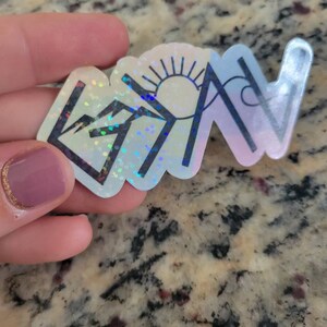 May include: A holographic sticker with a mountain, sun, and wave design. The sticker is iridescent and has a rainbow effect.