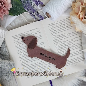 Peut inclure: Un marque-page en feutre marron en forme de dachshund avec le texte "book_lynni" et les mots "Nähzauberwäldchen" en bas.