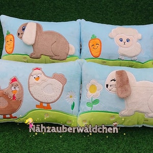 Può includere: Quattro cuscini di peluche blu e verdi con animali ricamati, tra cui un coniglio, un agnello, una gallina e una chioccia. I cuscini hanno uno sfondo blu chiaro con erba verde e fiori.