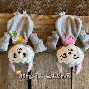 May include: Two gray plush bat toys with embroidered faces and wings. One bat has a pink heart and the other has a green leaf and orange and yellow patterned fabric.