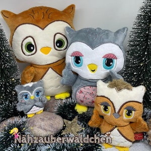 May include: Four plush owl toys in various colours and sizes. The largest owl is brown with white accents, the second largest is grey with white accents, the smallest is grey with white accents, and the smallest is brown with white accents. The owls are all sitting on a green and brown surface.