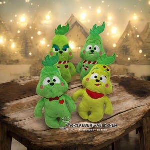 Puede incluir: Cuatro figuras de peluche en tonos verdes y amarillos, que se asemejan a un personaje de dibujos animados. Cada una tiene una cara distintiva, con rasgos bordados y un pequeño detalle en forma de hoja en la parte superior. Algunas figuras tienen detalles rojos como una pajarita o bufanda.