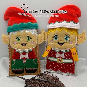 May include: Two Christmas elf-themed felt ornaments. One elf has green eyes, green pants, and a red jacket. The other elf has blue eyes and a red polka-dot dress. Both have red hats and elf ears. The text "Stickzauberwaeldchen Embroidery Design" is at the top.