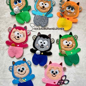 May include: A collection of colorful felt monster-shaped pouches. Each pouch features a unique design with different colors, facial expressions, and accessories. The text "Stickzauberwaeldchen Embroidery Design" is also visible.