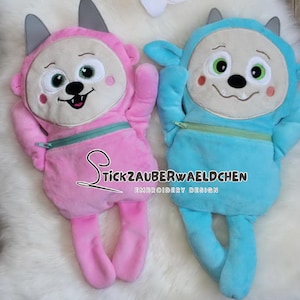 May include: Two plush monster dolls, one pink and one blue, with embroidered faces, ears, and limbs. Each doll has a zippered pocket and the text "Stickzauberwaeldchen Embroidery Design". They are lying on a white, fluffy surface.