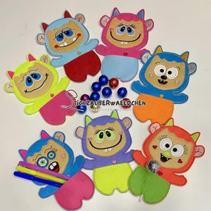 May include: A collection of colorful felt monster-shaped crafts. Each monster has a unique color scheme, with details like horns, eyes, and smiles. Some monsters hold candies or pens. The image includes the text "StickZauberwaeldchen Embroidery Design."