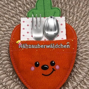 May include: A felt carrot-shaped utensil holder with a smiling face, green felt leaves, and a pink and white polka dot napkin inside. The holder is designed to hold a fork and spoon.