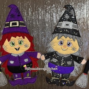 May include: Two felt witch dolls with purple and black clothing, black hats with spiderwebs, and brooms. The dolls have red and gray hair, and the text "Nahzauberwäldchen" is visible.