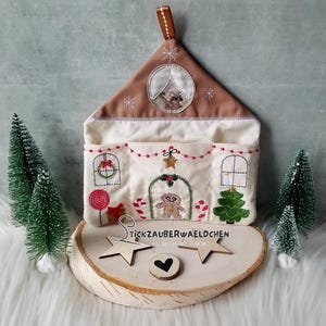 May include: A white fabric Christmas stocking shaped like a house with a brown roof and a gingerbread man design. The stocking has four pockets and is decorated with red and green embroidery.