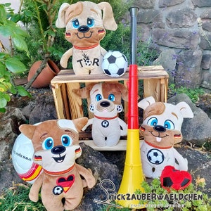 Puede incluir: Cuatro juguetes de peluche de perro con camisetas de fútbol y sosteniendo balones de fútbol. Los juguetes son marrones y blancos con ojos negros y narices rojas. Los juguetes están sentados en una caja de madera con un megáfono amarillo y rojo delante de ellos. El texto "STICKZAUBERWAELDCHEN EMBROIDERY DESIGN" es visible en la parte inferior de la imagen.
