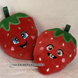 May include: Two plush red strawberry pillows with embroidered faces. One strawberry has a happy face with closed eyes and a wide smile. The other strawberry has a surprised expression with open eyes and a slightly open mouth.