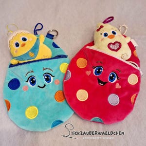 May include: Two plush, egg-shaped pouches with smiling faces and polka dots. One is teal with a yellow chick, the other is red with a yellow chick. Both have zippers and key rings. The pouches are embroidered with details.
