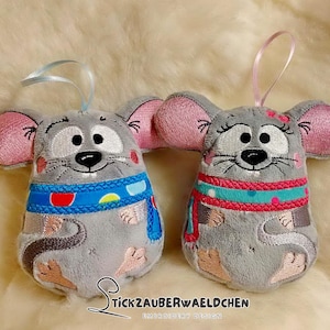 Puede incluir: Dos juguetes de peluche grises con forma de ratón con detalles bordados. Un ratón lleva una bufanda azul y roja con lunares blancos. El otro ratón lleva una bufanda rosa y azul con lunares blancos. Ambos ratones tienen orejas rosas y ojos negros.