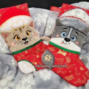 May include: Two Christmas stockings with embroidered animal faces. One stocking features a cat with a red Santa hat and the other features a dog with a white Santa hat. Both stockings have a red background with gold snowflakes and reindeer.