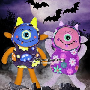 May include: Two plush monster dolls with one eye, one blue and one pink, stand in front of a full moon and bats. The blue monster has orange arms and legs, and the pink monster has lavender arms and legs. The dolls are on a graveyard background.