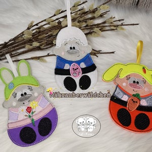 May include: Three felt finger puppets, each with a different animal design. The first puppet is a gray bunny wearing a green hat and a pink dress with a flower. The second puppet is a gray sheep wearing a blue shirt and a red hat. The third puppet is a yellow pig wearing a yellow hat and a red dress with a carrot. The puppets are all handmade and have embroidered details.