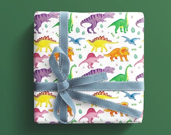 May include: A present wrapped in paper patterned with colourful dinosaurs on a white background. The dinosaurs are in shades of purple, green, yellow, orange, and pink. A light blue ribbon with a bow secures the gift, suitable for a birthday or special occasion.