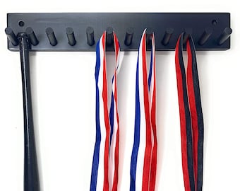 May include: A black wooden wall-mounted medal display with nine hooks. Three medals with red, white, and blue ribbons are hanging on the hooks. A black baseball bat with the text "Tampa Bay Rays" is hanging on the left side of the display.