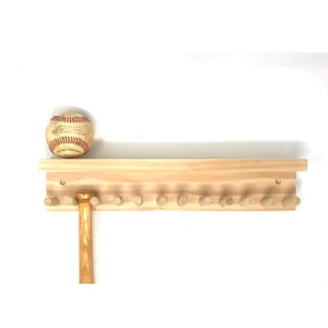 May include: A wooden baseball bat and ball holder with a shelf. The holder has 12 pegs for bats and a shelf for balls. The holder is made of natural wood and has a rustic look.