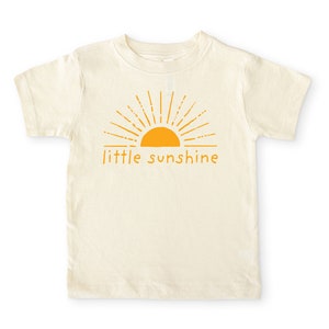 Natural cream colored short sleeve toddler crew neck shirt with mustard yellow little sunshine text print with boho sun rays design, laying flat on white background