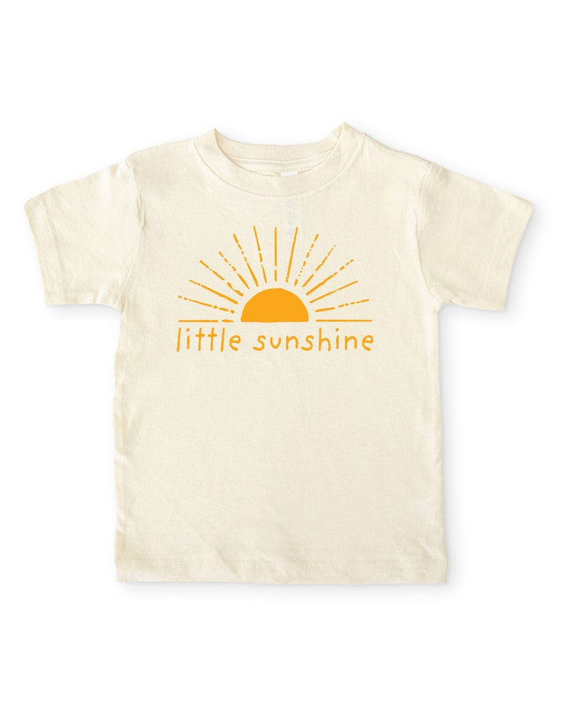 Natural cream colored short sleeve toddler crew neck shirt with mustard yellow little sunshine text print with boho sun rays design, laying flat on white background