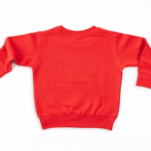 Back view of red long sleeve toddler fleece sweatshirt laying flat on white background